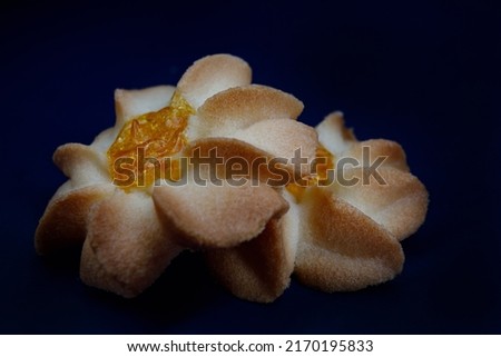 Two shortbread cookies in close - up on a dark red background . Kurabye cookies with jam . Beautiful cookies in the shape of a flower side view.