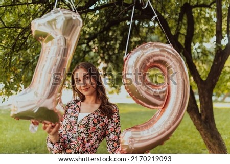 a photo of a teenage girl being photographed next to a birthday number in the park. High quality photo