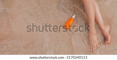 Close-up of young female bare feet with sunscreen cream on beach with a sea wave. Woman uses moisturizer, relaxing, enjoying time of summer vacation. Legs of girl on the seaside with sandy background Royalty-Free Stock Photo #2170240113