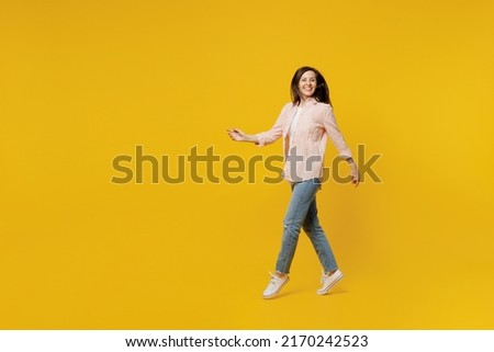 Full size side view young happy smiling woman she 30s wear striped shirt white t-shirt walking going strolling look camera isolated on plain yellow background studio portrait. People lifestyle concept