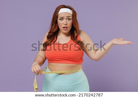 Young confused sad indignant chubby overweight plus size big fat fit woman in top hold measure tape waist spread hand warm up train isolated on purple color background home gym Workout sport concept. Royalty-Free Stock Photo #2170242787
