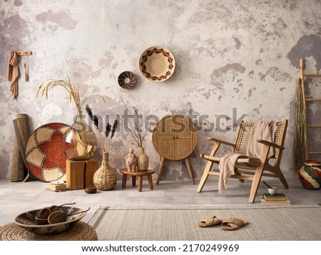 The stylish ethnic composition at living room interior with design brown armchair, colorful baskets, rattan sideboard and elegant personal accessories. Grey concrete wall. Cozy apartment. Home decor.  Royalty-Free Stock Photo #2170249969