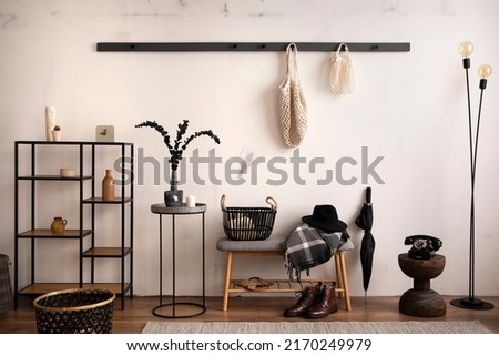 The stylish composition of cosy entryway with grey bench, black consola, hanger and lamp. Beige wall. Home decor. Template. 