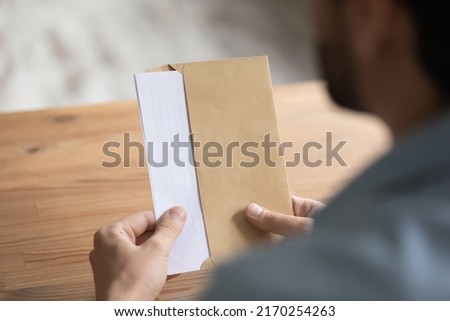 Man sit at table opens envelope with letter or post card inside, close up view over male shoulder. Paper correspondence with information, bank notification, paperwork at workplace, invitation concept Royalty-Free Stock Photo #2170254263
