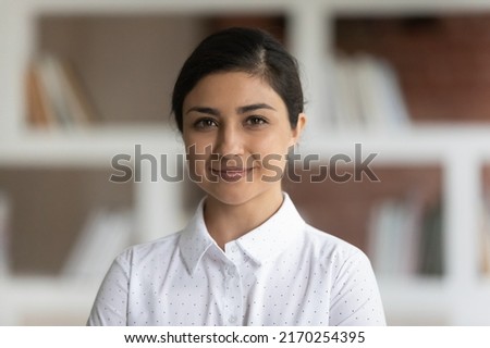 University or school teacher, business lady had shot portrait concept. Young attractive Indian ethnicity woman in white shirt pose in library room with bookshelves on background smile look at camera