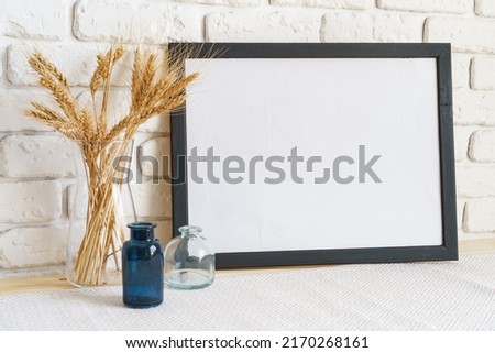 Vase with ears of wheat and photo frames against brick wall, close up
