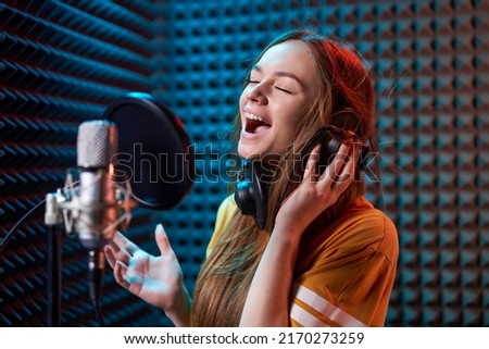 Girl in recording studio singing with mic in headphones , over acoustic absorber panel background. Emotional with closed eyes