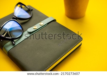 Office concept. Pair of glasses, notebook, cup of coffee on a yellow background
