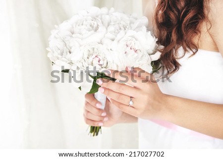 Bride holding wedding bouquet of white peonies on light background