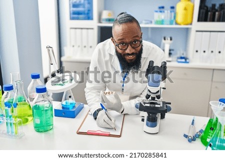 Young african american man wearing scientist uniform writing on clipboard at laboratory