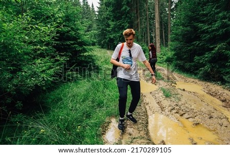 Couple of young people in casual clothes walk in a hike on a forest road with puddles and swamp. Group of people walking on a mountain road with a swamp stepping over puddles. Royalty-Free Stock Photo #2170289105