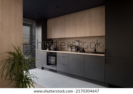 Modern and elegant kitchen, with black and wooden cupboards and big window with blinds Royalty-Free Stock Photo #2170304647