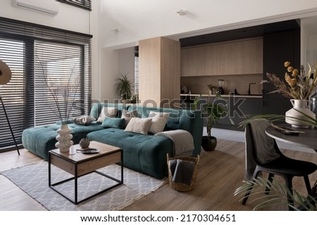 Big, blue and cozy corner sofa in modern living room with big windows open to dark kitchen Royalty-Free Stock Photo #2170304651