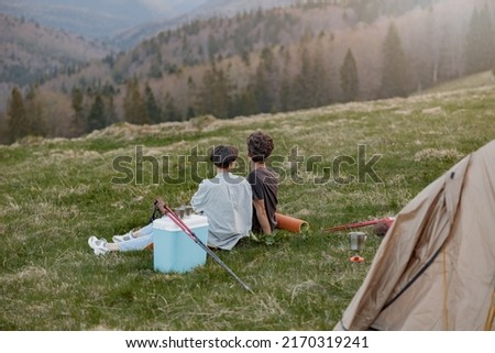 Rear of romantic couple sitting on grass at tent high in mountains. Beautiful view.