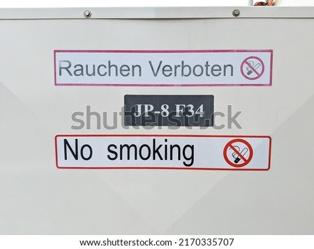 No smoking sign in English and German. Outdoor sign prohibiting smoking in red and white