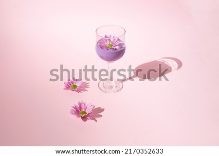 Aesthetic scene with pink daisy flowers and wine glass full of purple liquid. Sun and shadow. 