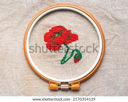 red poppy flower in plastic hoop embroidered by hand on fabric close up