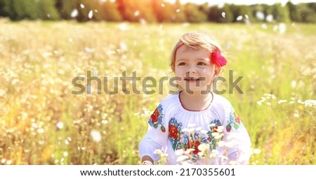 Banner with a happy little Ukrainian Caucasian girl in a shirt with embroidery walking in a field of chamomile. In the country. Stunning nature background at sunset. Summer concept