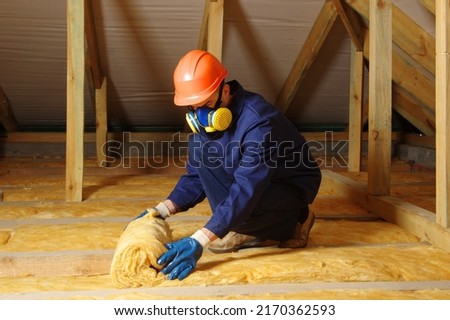 Construction worker thermally insulating house attic with glass wool  Royalty-Free Stock Photo #2170362593