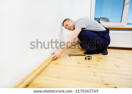 To make repairs. Installing a new skirting board. a man makes repairs in a room Royalty-Free Stock Photo #2170363769