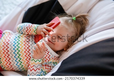 Cute little toddler girl playing with smartphone Healthy baby touching mobile phone with fingers, looking cartoons and having fun with educational apps. Child smiling
