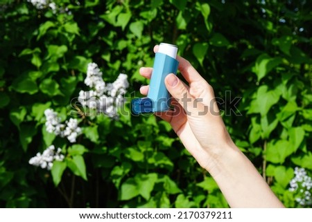 Pharmaceutical drug for the relief of an asthma attack. The hand of a young woman holds a blue inhaler for asthma. Health and medical concept.