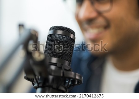 Close-up content creator man host streaming a podcast on laptop set up with headphones and condenser microphone interview guest conversation at broadcast studio. Blogger recording voice over radio
