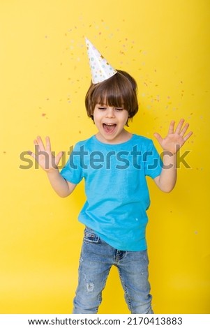 Handsome Little birthday boy in blue shirt and hat with balloons, yellow background, happy birthday. High quality photo