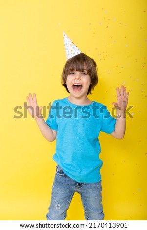 Handsome Little birthday boy in blue shirt and hat with balloons, yellow background, happy birthday. High quality photo