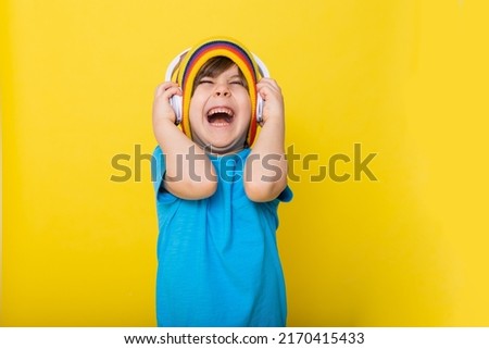 Handsome little boy in blue shirt and colorful hat with headphones, yellow background. High quality photo