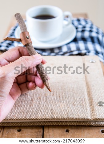 Hand holding rustic pencil  on notebook with coffee cup background