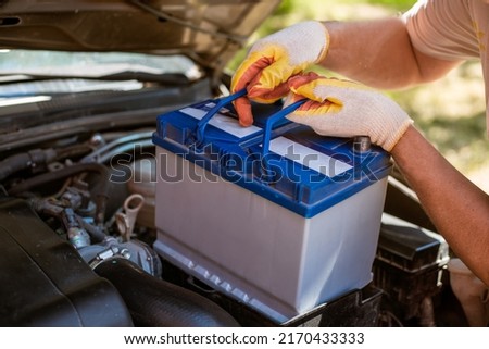 A man removes a battery from under the hood of a car. Battery replacement and repair. Royalty-Free Stock Photo #2170433333