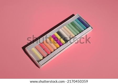 colored pastel crayons in a box on a pink background