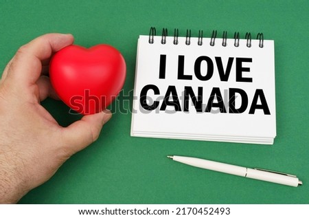 On the green surface are a pen, a notepad with the inscription - I love Canada. A man has a heart in his hands.