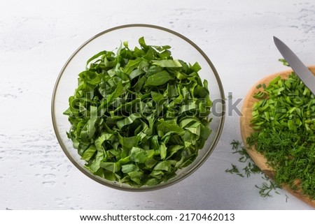 Glass bowl with chopped spinach and a board with onion and dill on a light blue background, top view. Cooking healthy vegan food Royalty-Free Stock Photo #2170462013