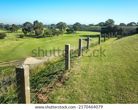 Plain wire fence with wooden posts of a golf course with a background of large green grassy lawn. Copy space for text. 