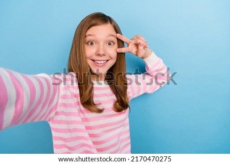 Photo of funny charming girl make selfie fingers make v-sign near eye isolated on blue color background