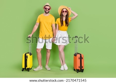 Full size photo of two idyllic cheerful partners hold hands suitcase flight isolated on green color background