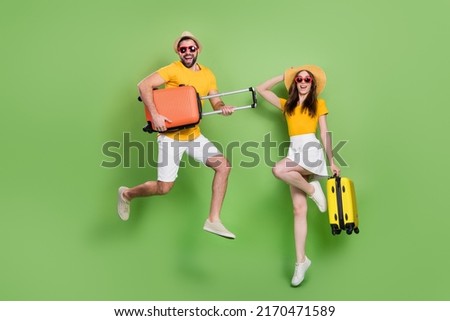 Full size photo of two excited energetic people jumping hold suitcase isolated on green color background