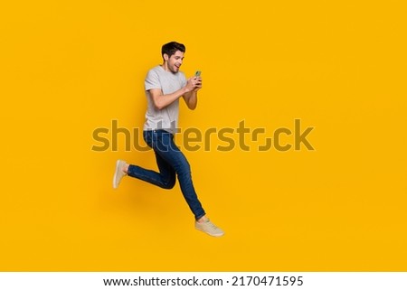 Full length body size view of attractive cheerful guy jumping using device running isolated over vivid yellow color background