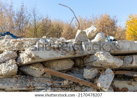 Fragments of concrete walls. Destroyed building or dismantled building. Concrete debris against the background of autumn trees. Rusty building rebar