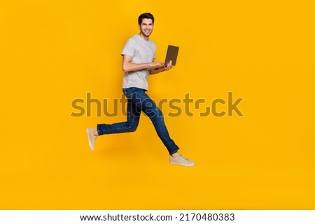 Full size profile photo of funky brunet young guy run type laptop wear t-shirt jeans sneakers isolated on yellow background