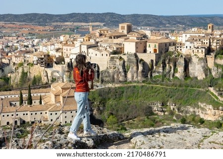 Woman tourist takes pictures of the picturesque houses on the cliff edge of the city of Cuenca. Spain