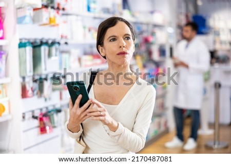 Portrait of positive young adult woman consumer using smartphone at pharmacy