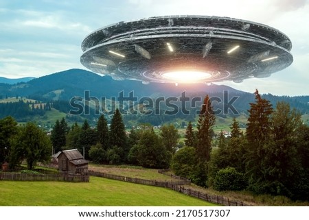 UFO, an alien saucer hovering above the field in the clouds, hovering motionless in the sky. Unidentified flying object, alien invasion, extraterrestrial life, space travel, spaceship. mixed media Royalty-Free Stock Photo #2170517307