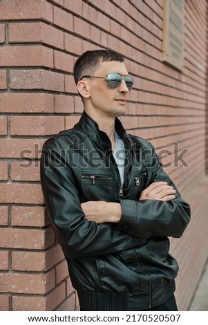 handsome thin guy leaned against the wall, red brick, leather jacket