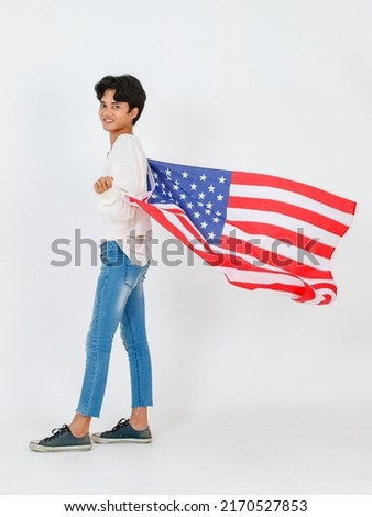 Portrait studio shot of Asian young LGBT gay bisexual homosexual male fashionable model in casual outfit and fashion sunglasses standing holding waving flying USA national flag on white background.