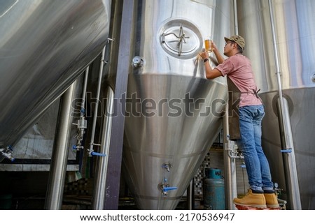 Young male brewer holding a glass of beer in hand Check out the taste and color of the beers in his craft beer brewery.