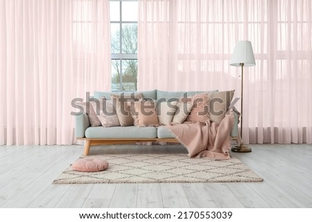 Grey sofa with soft pillows and lamp near big window with pink curtains in living room Royalty-Free Stock Photo #2170553039