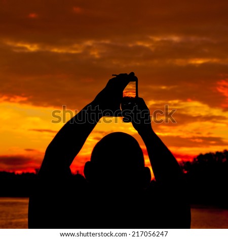 Silhoettes of people taking pictures of burning sunset sky horizon